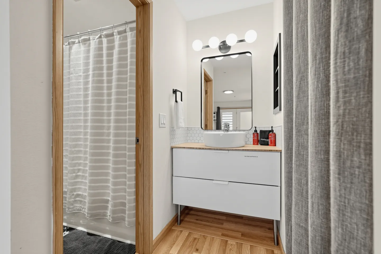 Bathroom vanity with a round vessel sink, illuminated mirror, and an adjacent shower area with a striped curtain.