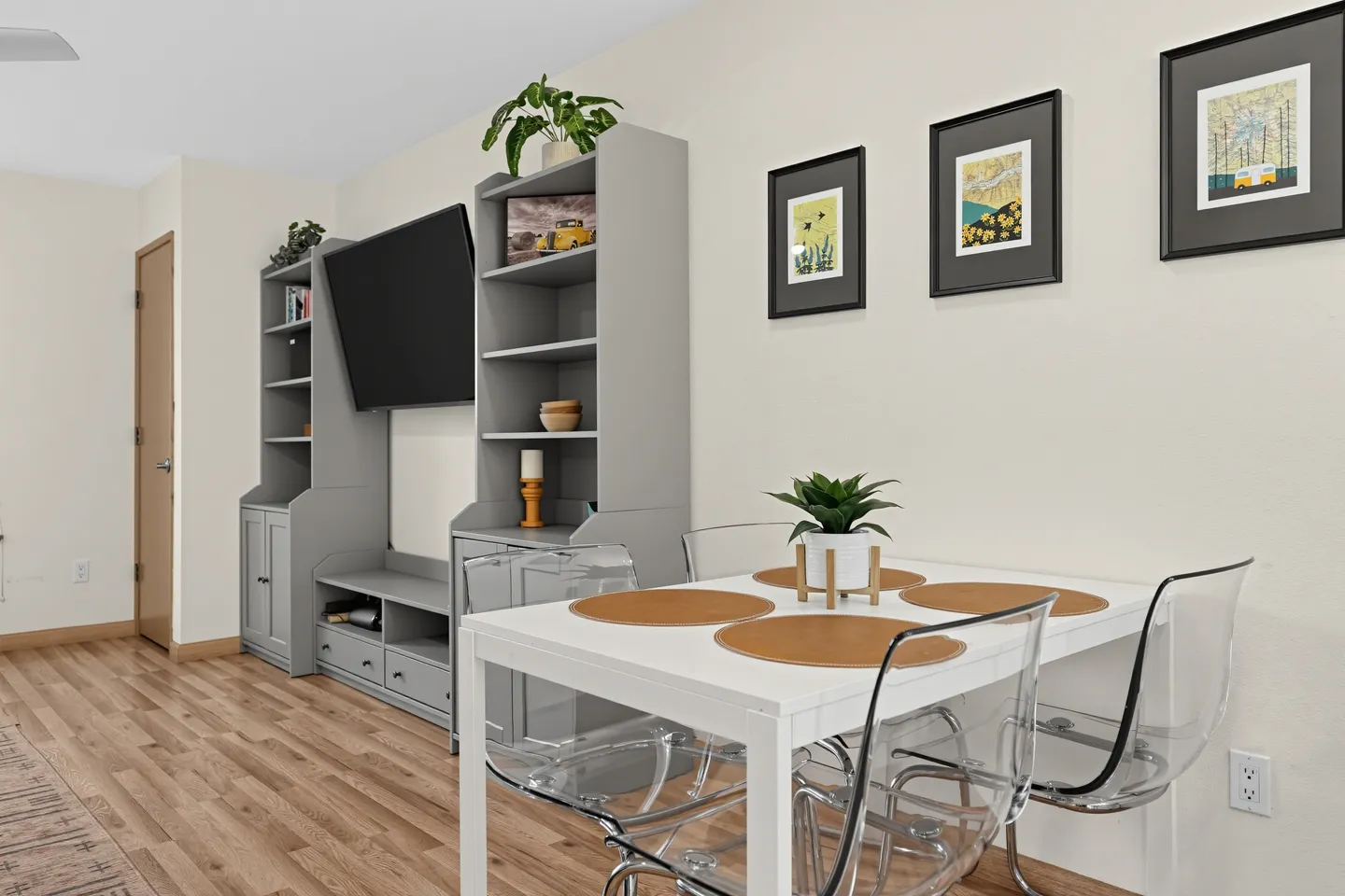 Dining table with clear chairs in front of a gray entertainment center with a mounted TV.