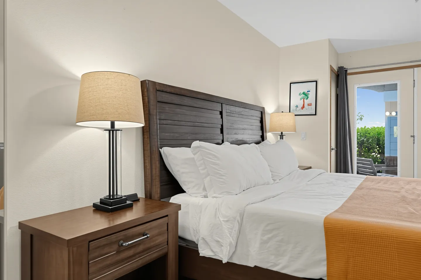 Bedroom featuring a wooden headboard, white bedding with an orange runner, matching nightstands with lamps, and a glass door leading outside.