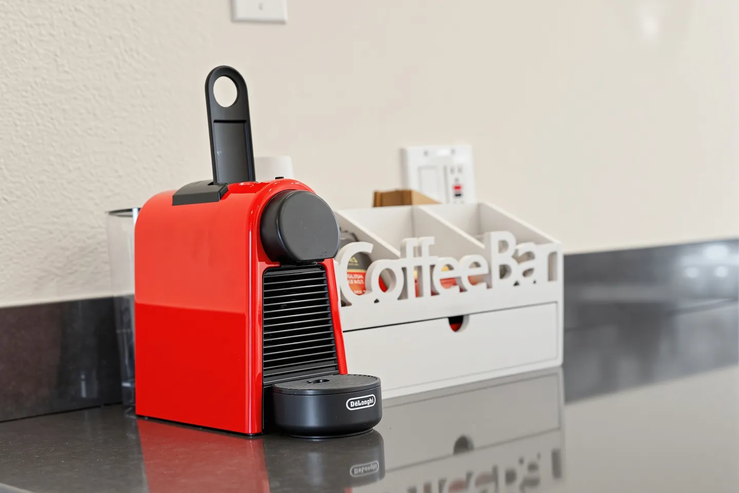 Close-up of a red espresso machine and a white organizer labeled 'Coffee Bar' on a dark countertop.