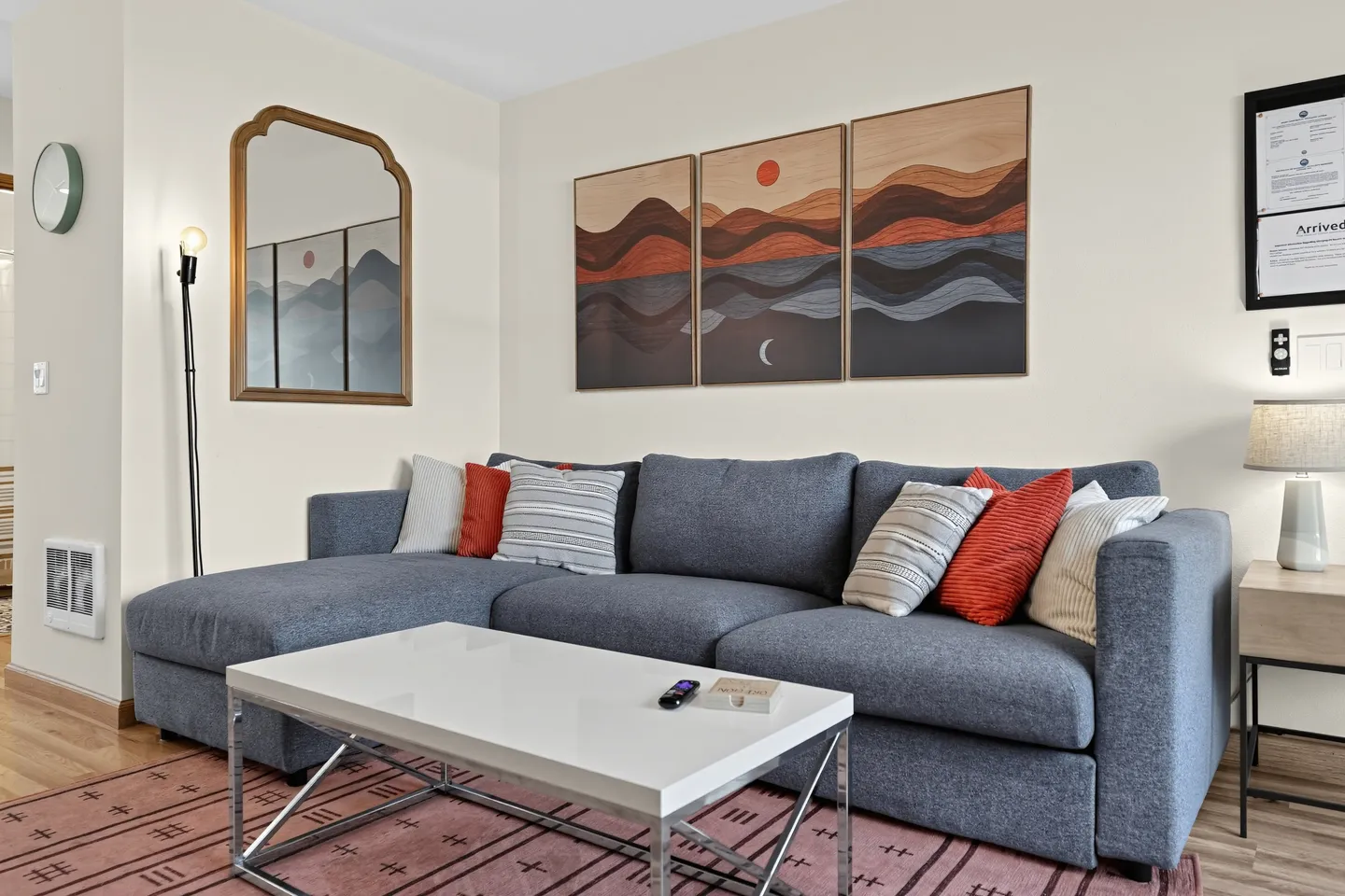Living room seating area with a blue sectional sofa, coffee table, patterned rug, and wall art.