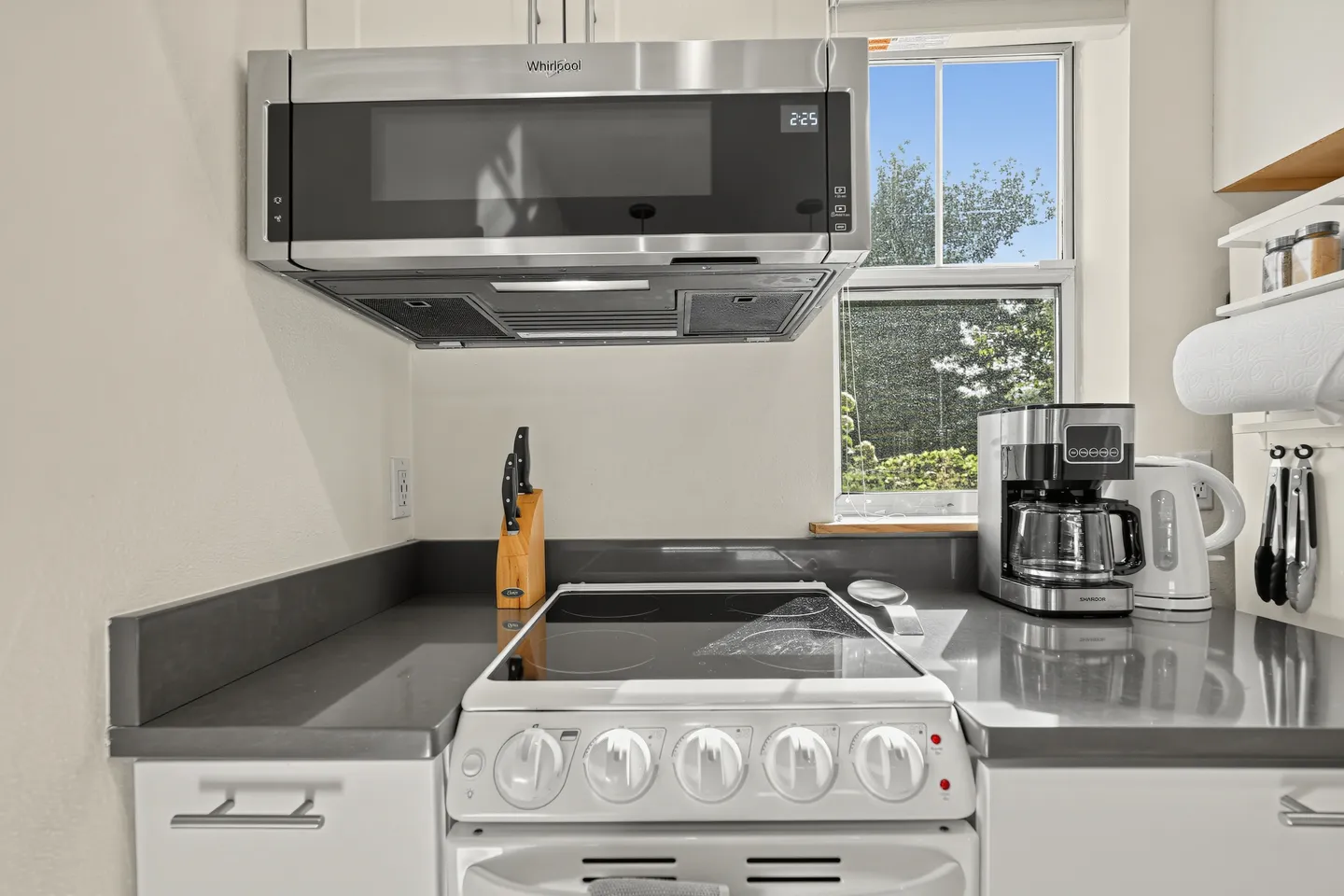 Kitchen counter area with an electric range, over-the-range microwave, knife block, and coffee maker near a window.