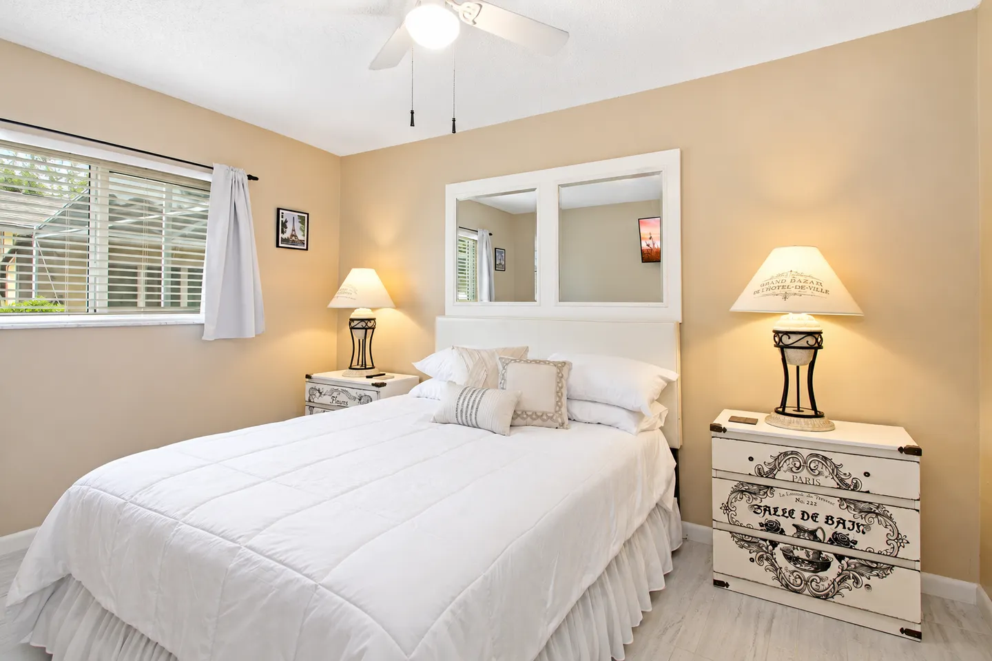 Bedroom with a white-dressed bed, matching nightstands with lamps, and a window with blinds.