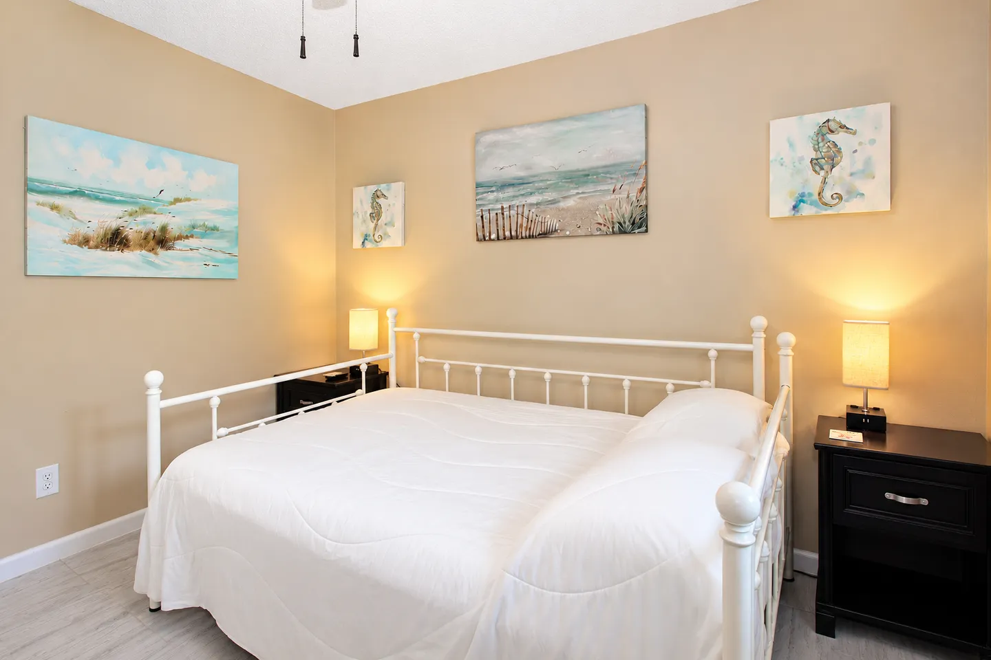 Bedroom with a white metal daybed, coastal wall art, and two black nightstands with lamps.