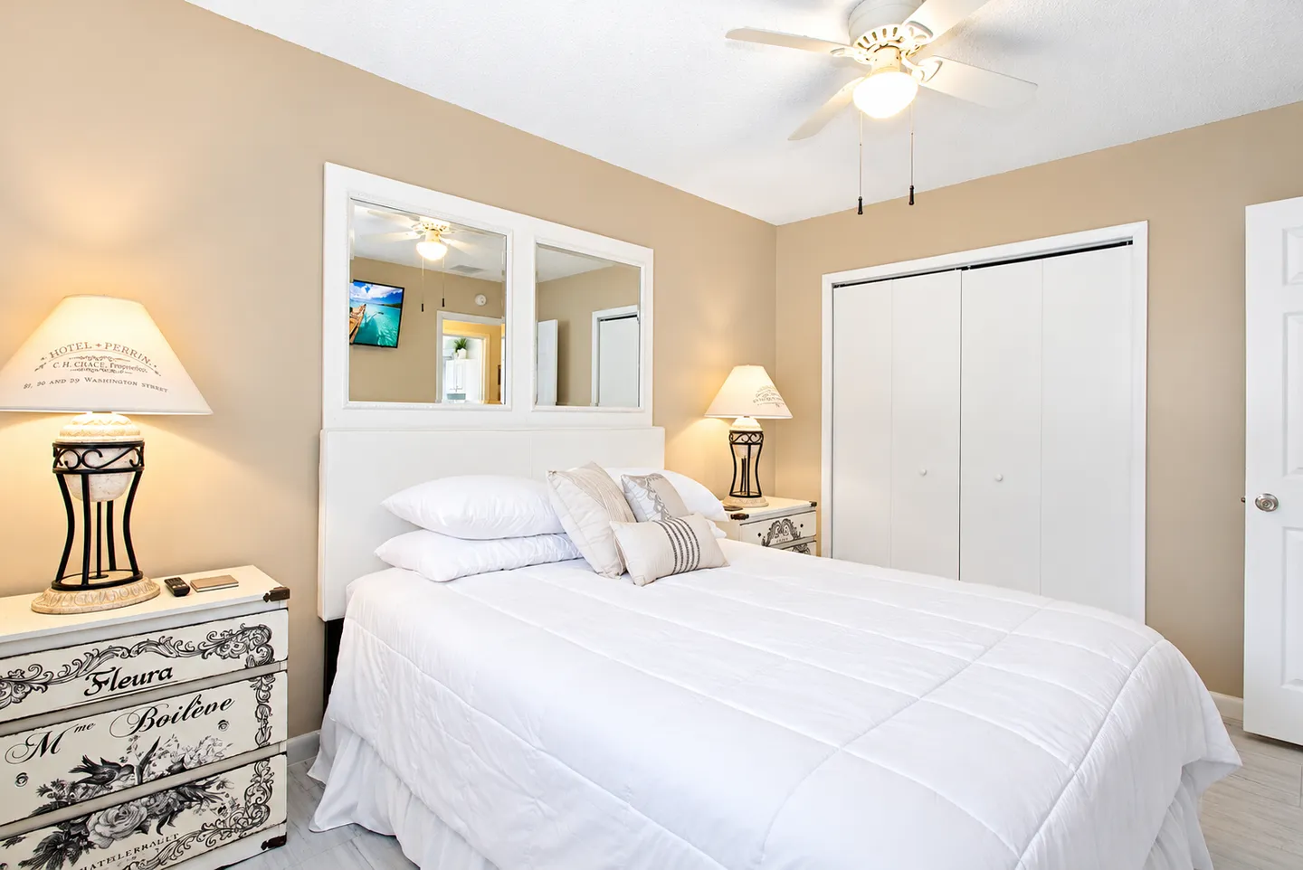 Bedroom with a white-dressed bed flanked by nightstands with matching lamps, mirrored wall accents, and a closet with bifold doors.