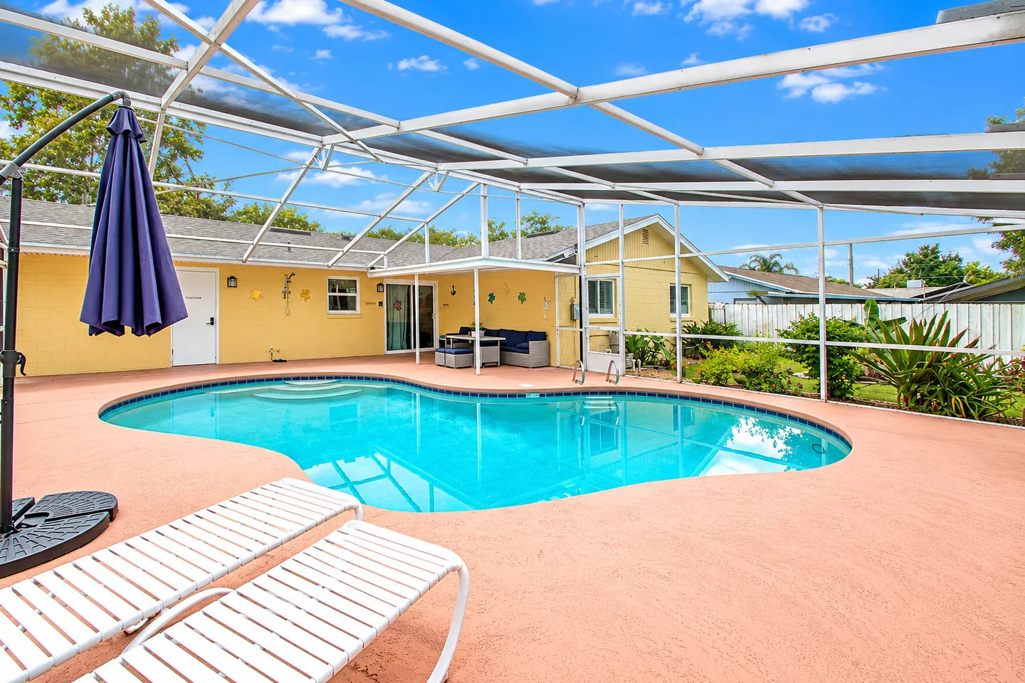 Screened-in outdoor swimming pool behind a yellow single-story home with patio furniture and lounge chairs.