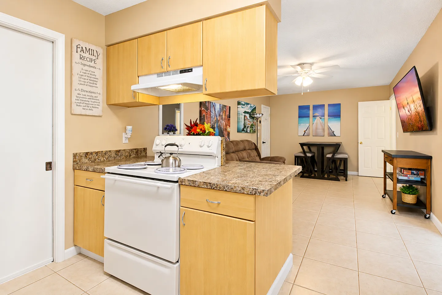 Kitchen counter and white electric stove with an open view into the living and dining areas featuring tile flooring.