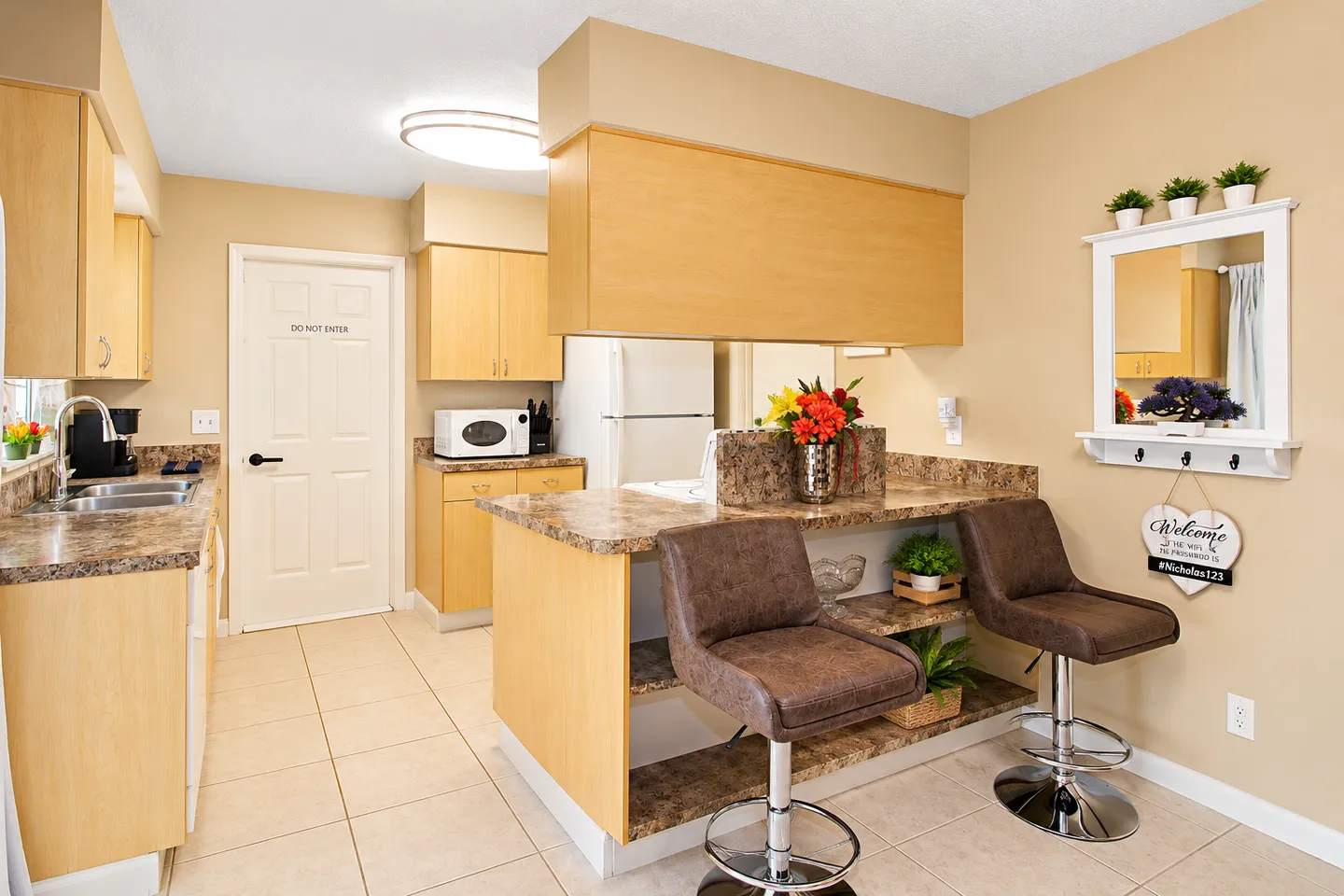 Kitchen featuring a breakfast bar with two leather barstools, light wood cabinets, and tiled flooring.