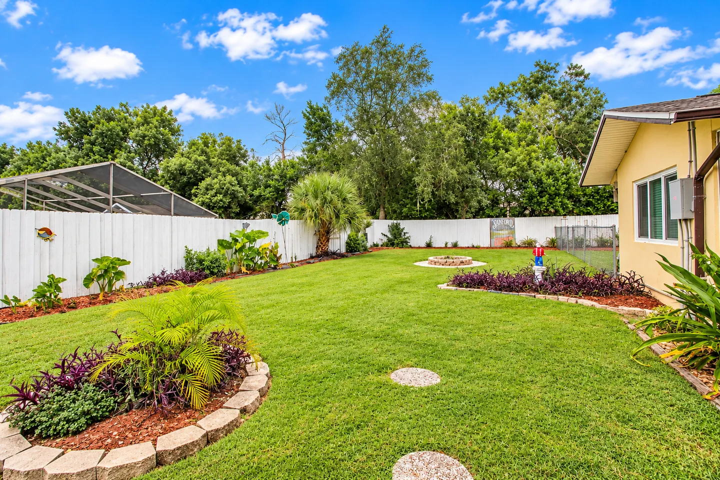 A fenced backyard lawn with landscaped mulch garden beds and stone borders on a sunny day.
