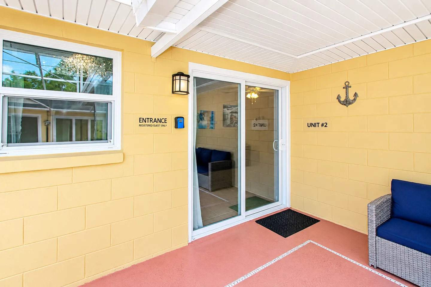 Exterior covered entrance labeled Unit #2 with yellow painted concrete block walls, sliding glass door, and outdoor seating.