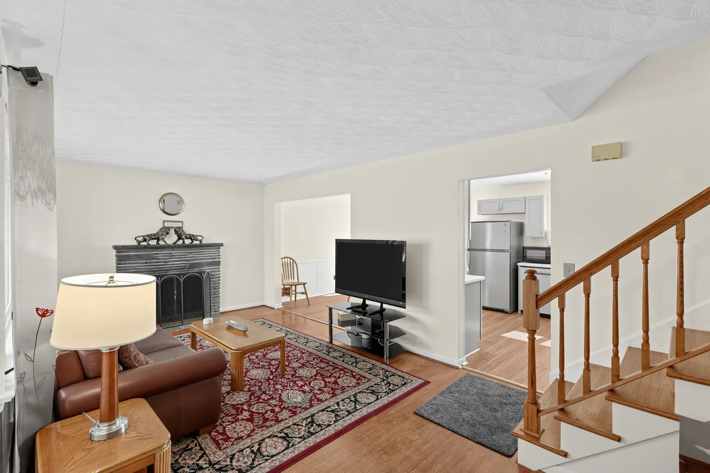 Living room featuring a brown sofa, patterned area rug, coffee table, fireplace, television, and stairs.