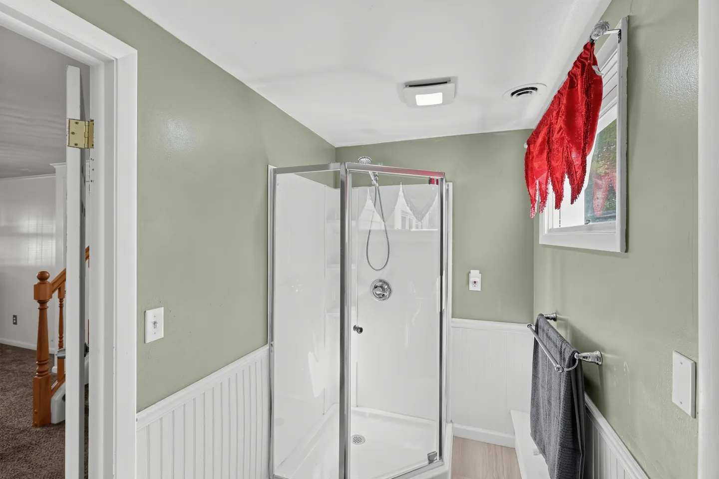 Bathroom with sage green walls, white wainscoting, and a corner glass-enclosed shower.