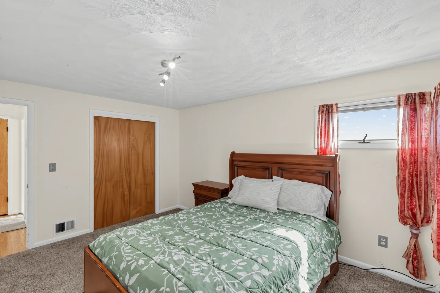 Bedroom with a wooden bed dressed in green patterned bedding, carpeted flooring, and a sliding closet door.