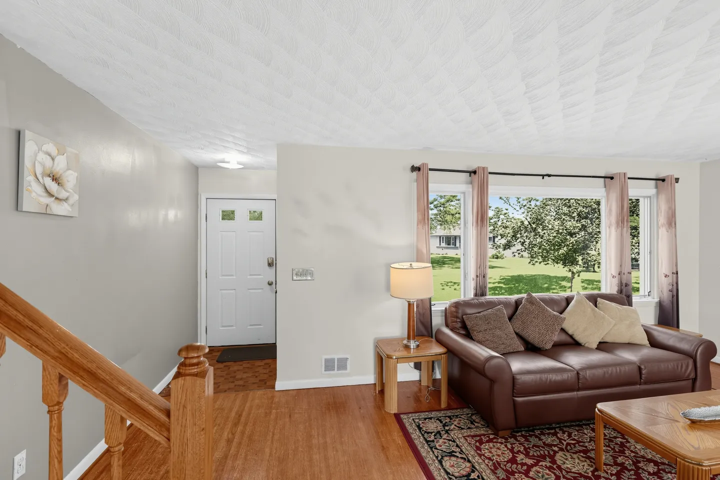 Living room and entryway with brown leather couch, textured ceiling, wooden floors, and front door.