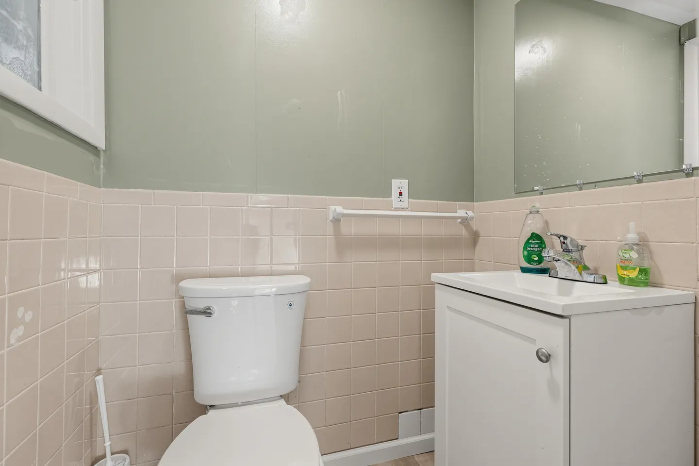 Bathroom showing a white toilet, white vanity sink, pink wall tile, and a frameless mirror.