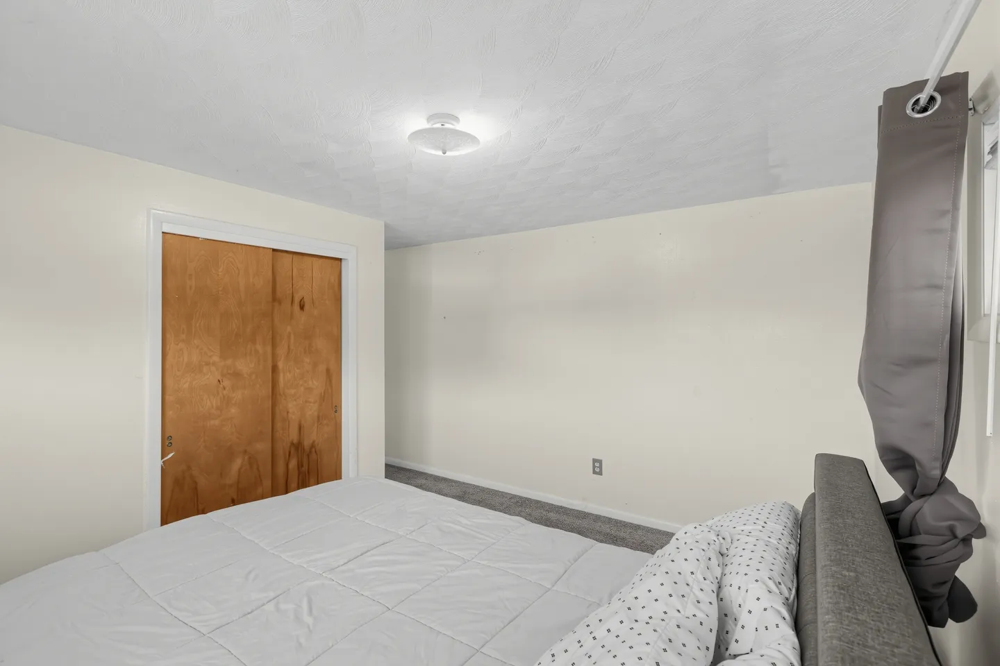 Bedroom featuring a made bed with gray headboard, carpeted floor, light walls, and a wooden sliding closet door.