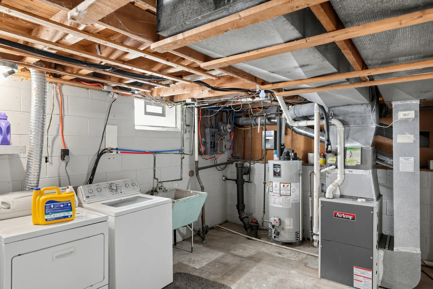 Unfinished basement utility area with washer, dryer, utility sink, water heater, and furnace.