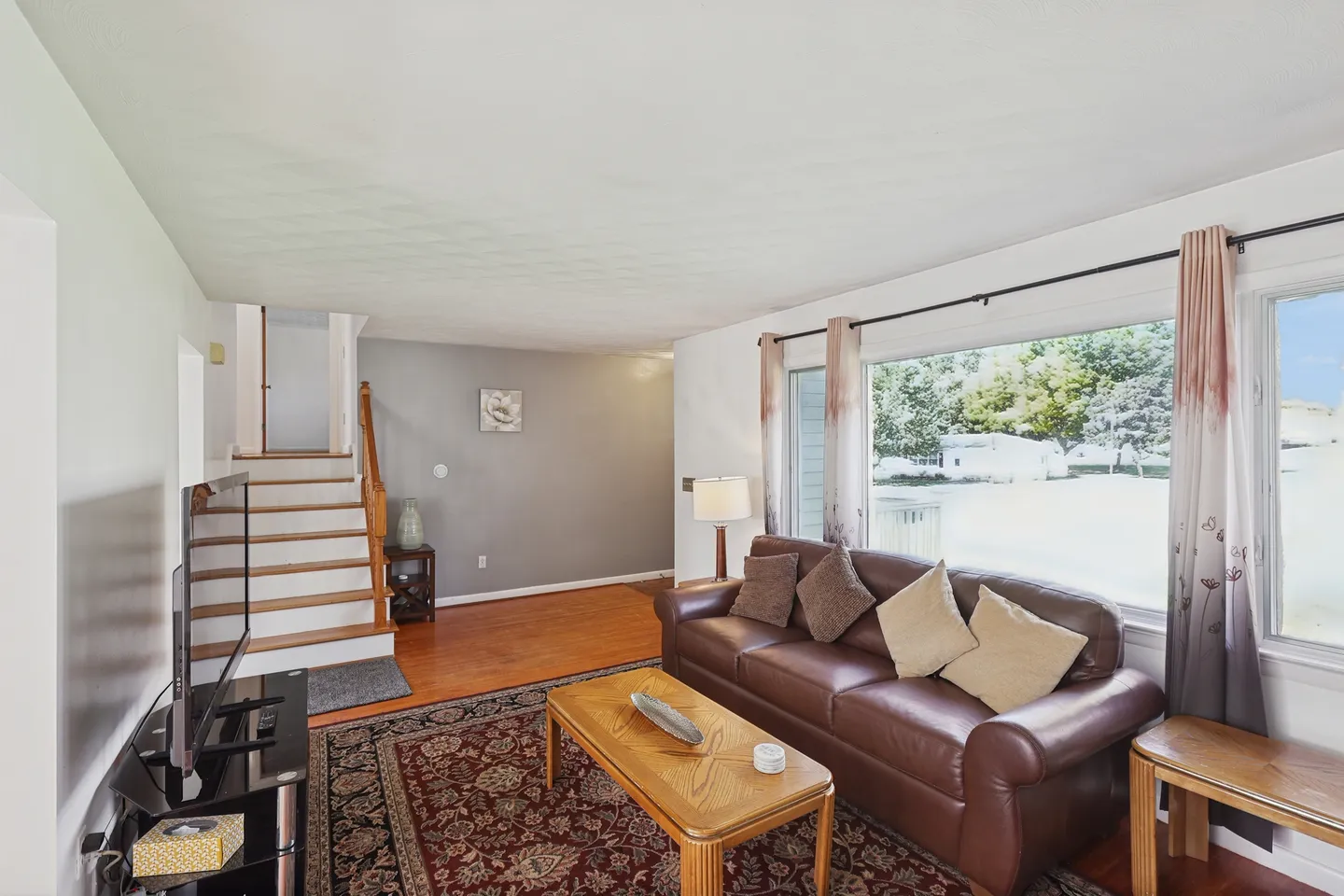 Living room featuring a brown leather sofa, patterned rug, wooden coffee table, television, and stairs leading up.