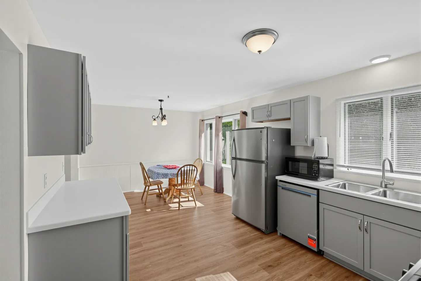 Open kitchen and dining area with grey cabinets, stainless steel refrigerator, and wood-look flooring.