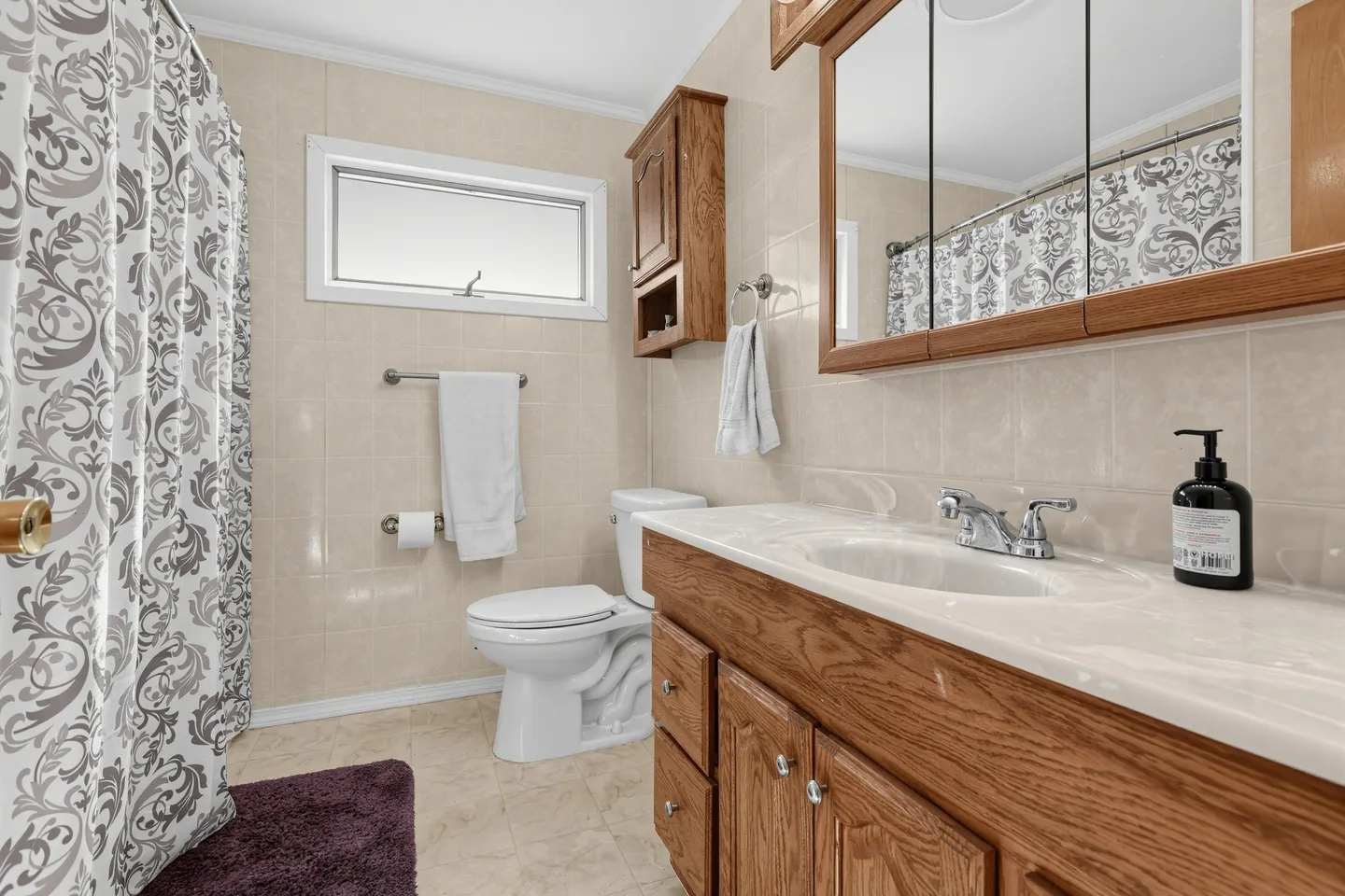 Bathroom with oak vanity, tiled walls, toilet, and patterned shower curtain.