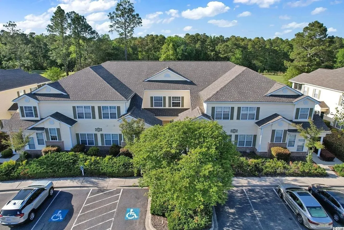 Aerial view of a two-story multi-unit residential building with a parking lot in front and green trees in the background.