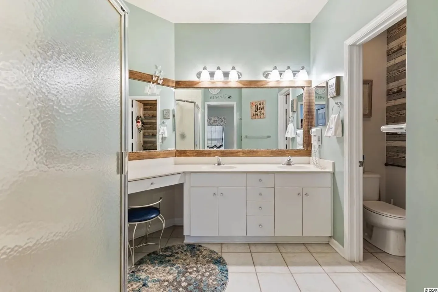 Bathroom with a double-sink white vanity, large framed mirrors, seated vanity area, and tiled flooring.