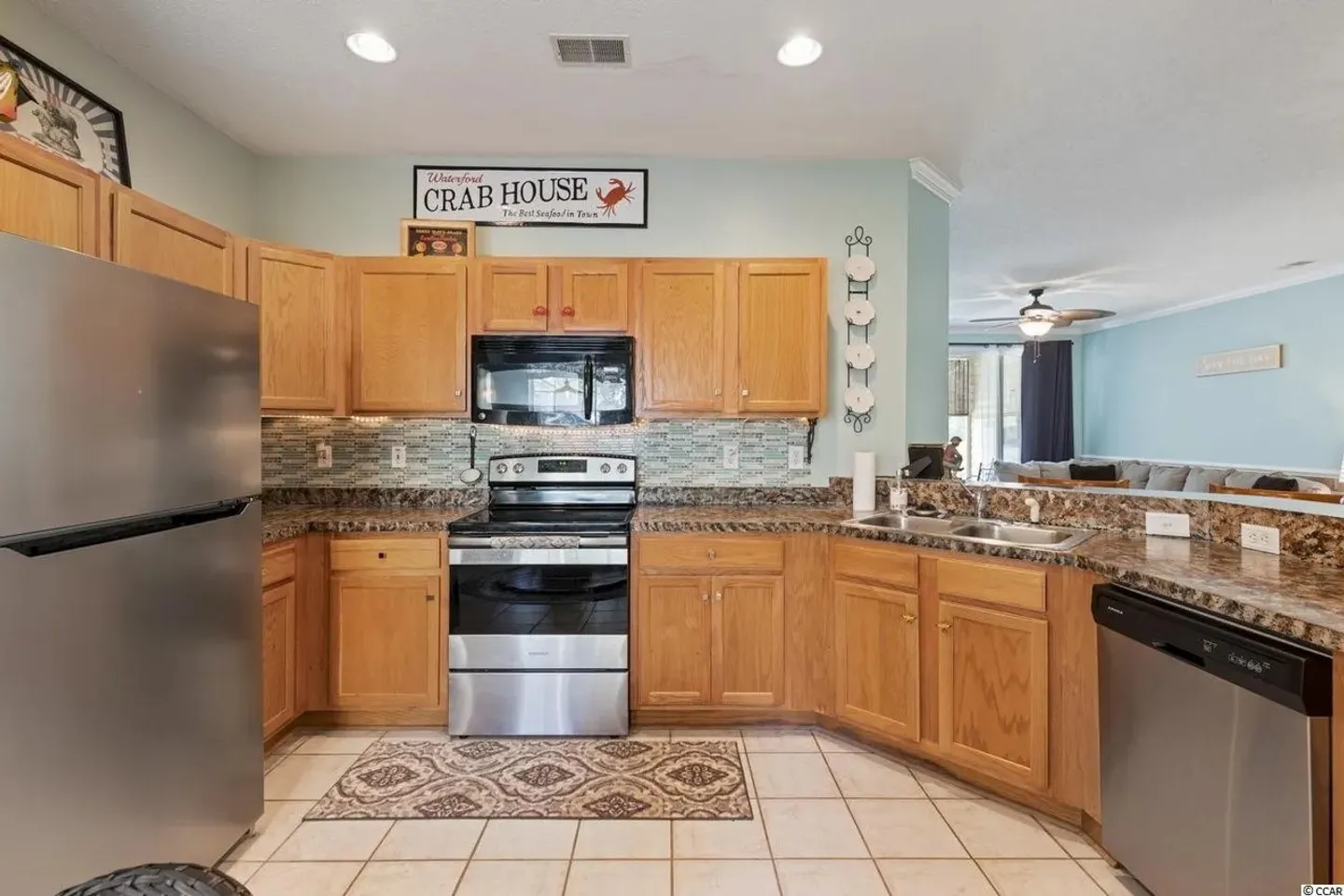 Kitchen with light wood cabinetry, stainless steel appliances, speckled countertops, and tile flooring.