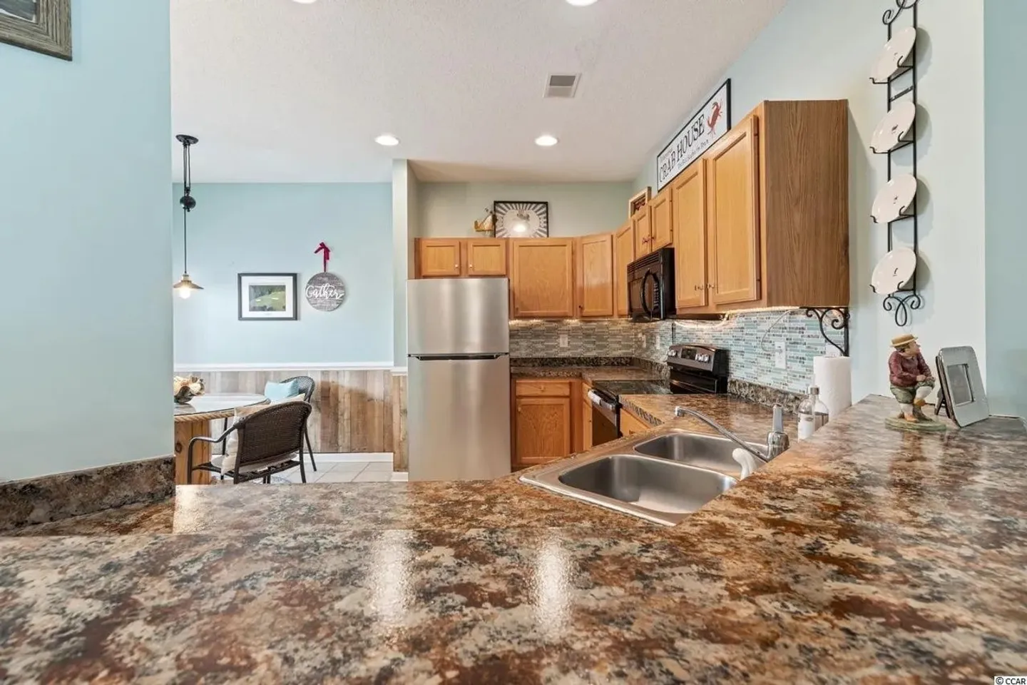 Kitchen with brown patterned countertops, wooden cabinets, stainless steel refrigerator, and a view into the dining area.