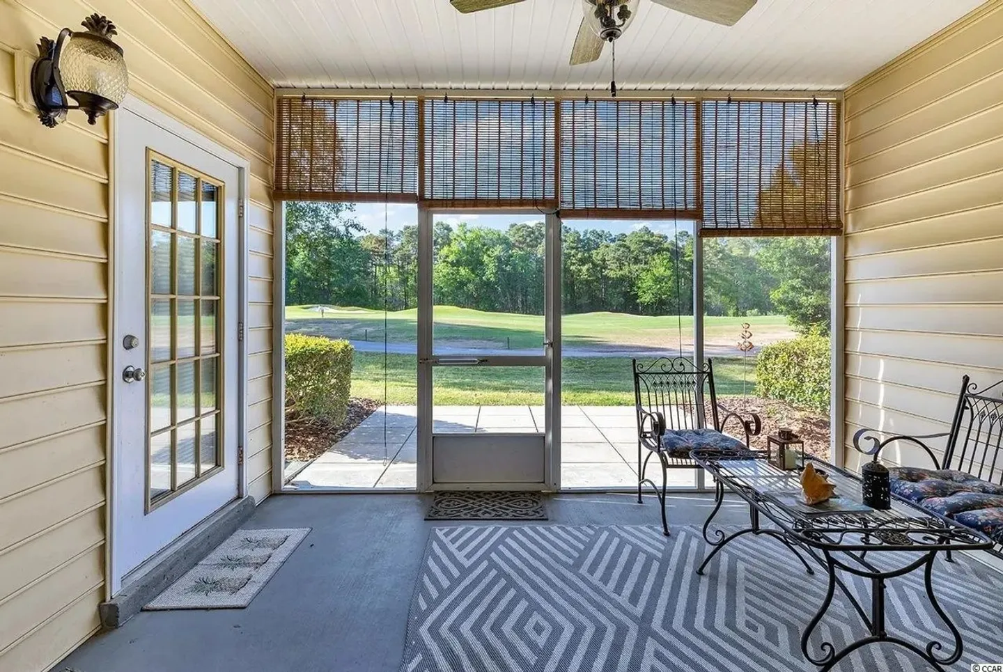 Screened-in porch with outdoor seating, woven shades, and views of a green lawn and golf course beyond.