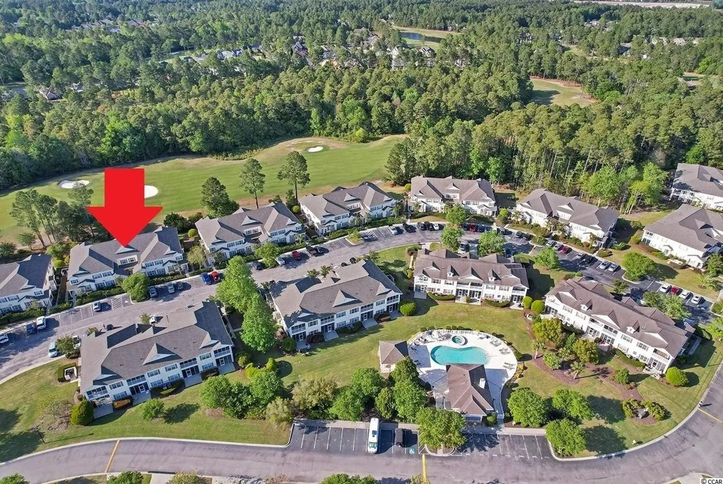 Aerial view of a residential complex with buildings, parking lots, a swimming pool, and an adjacent golf course.