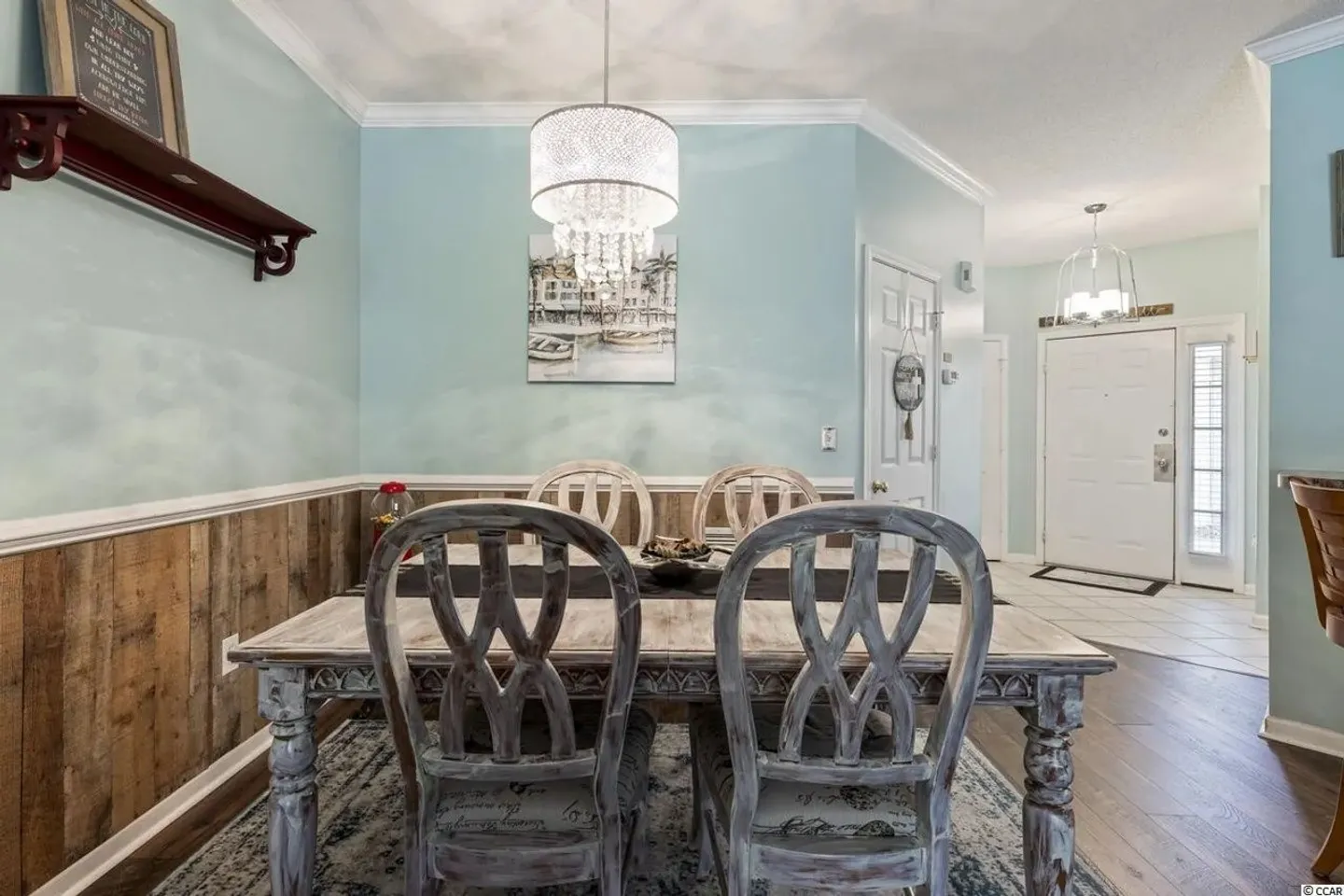 Dining area featuring a rustic distressed wood table and matching chairs under a crystal chandelier, next to an entryway.