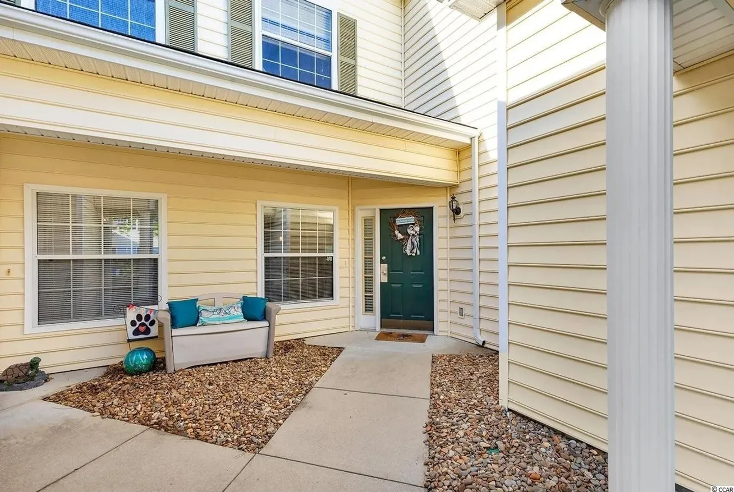 Covered front entry of a pale yellow vinyl-sided home with a dark green front door and concrete walkway.