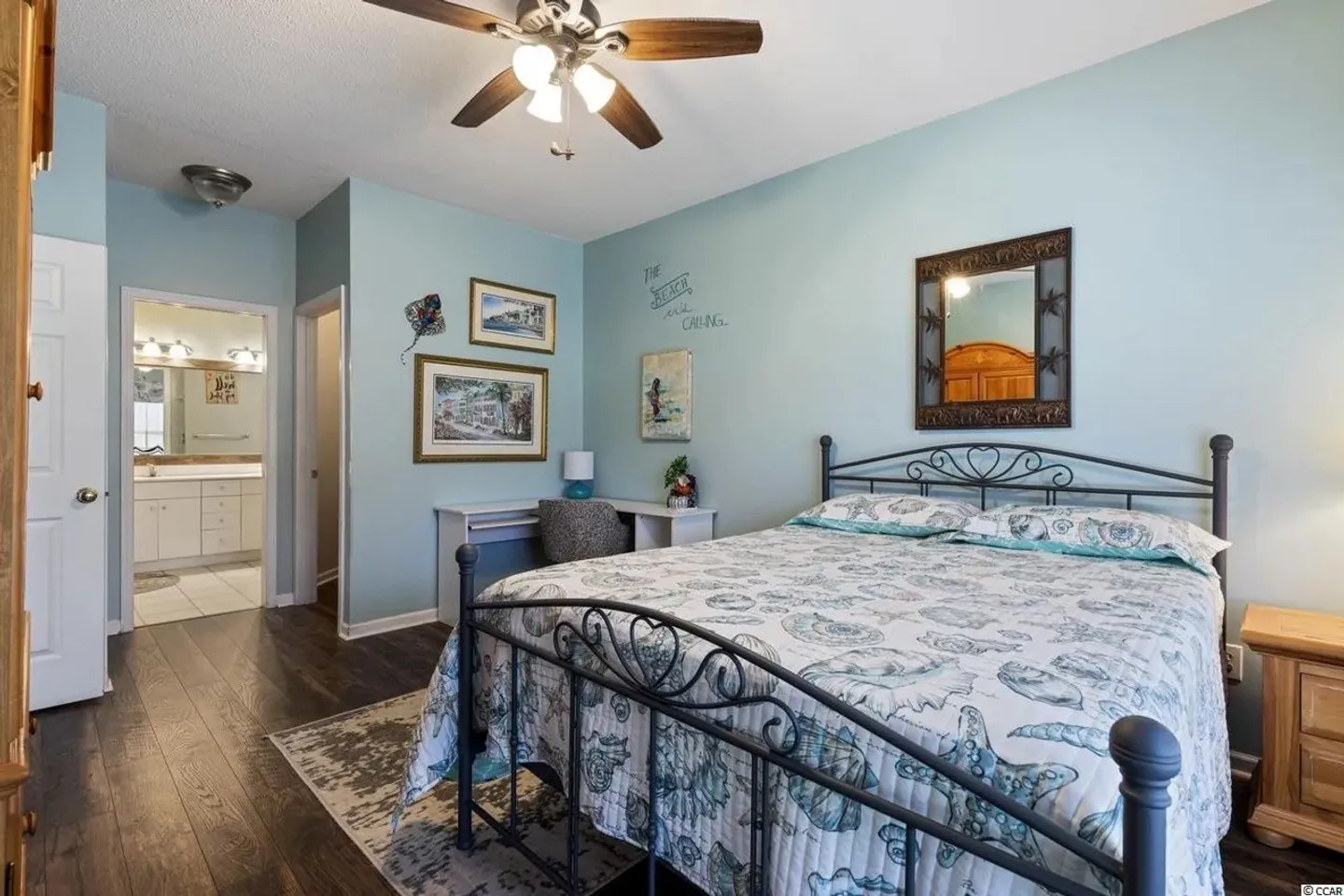 Bedroom with blue walls, dark wood-style floors, a wrought-iron style bed frame, and an open doorway leading into an en suite bathroom.