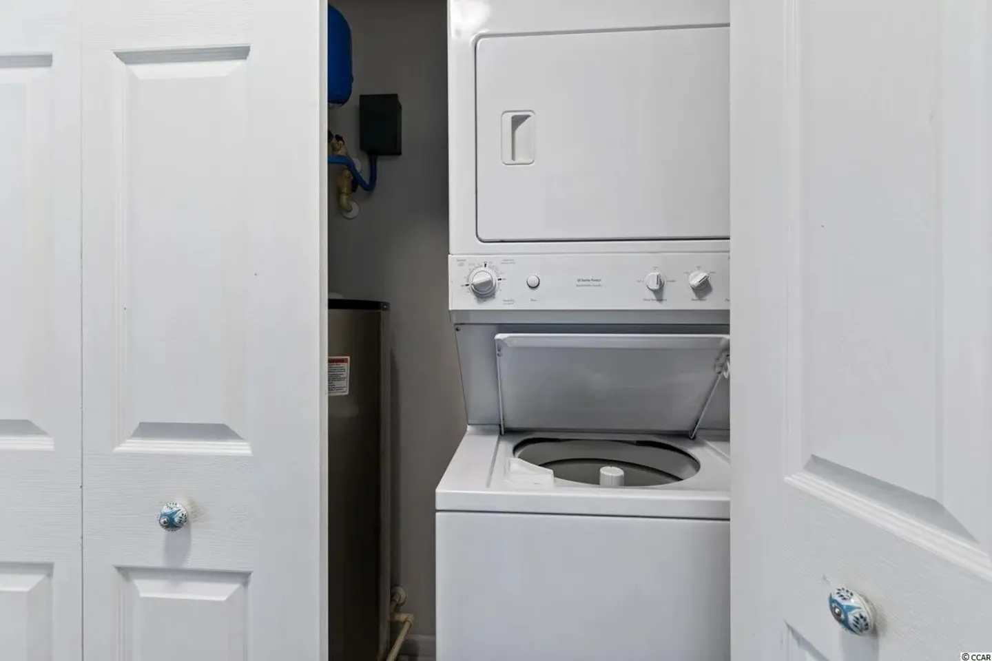 A stacked white washer and dryer unit inside a closet with bifold doors.
