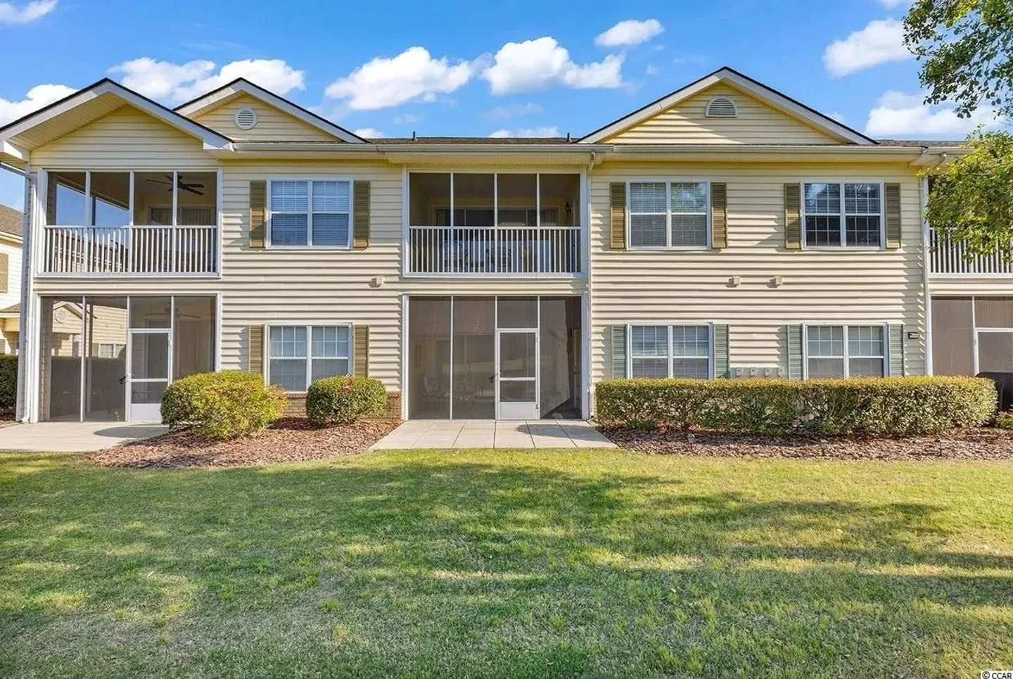 Exterior rear view of a two-story light yellow condo building with screened-in porches and a grassy lawn.
