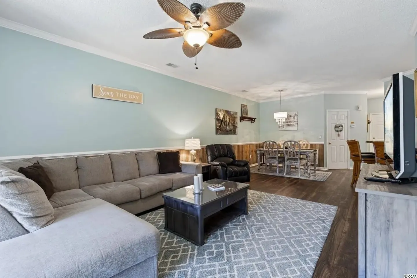 Open-concept living room and dining area featuring a sectional sofa, coffee table, ceiling fan, and dining set in the background.