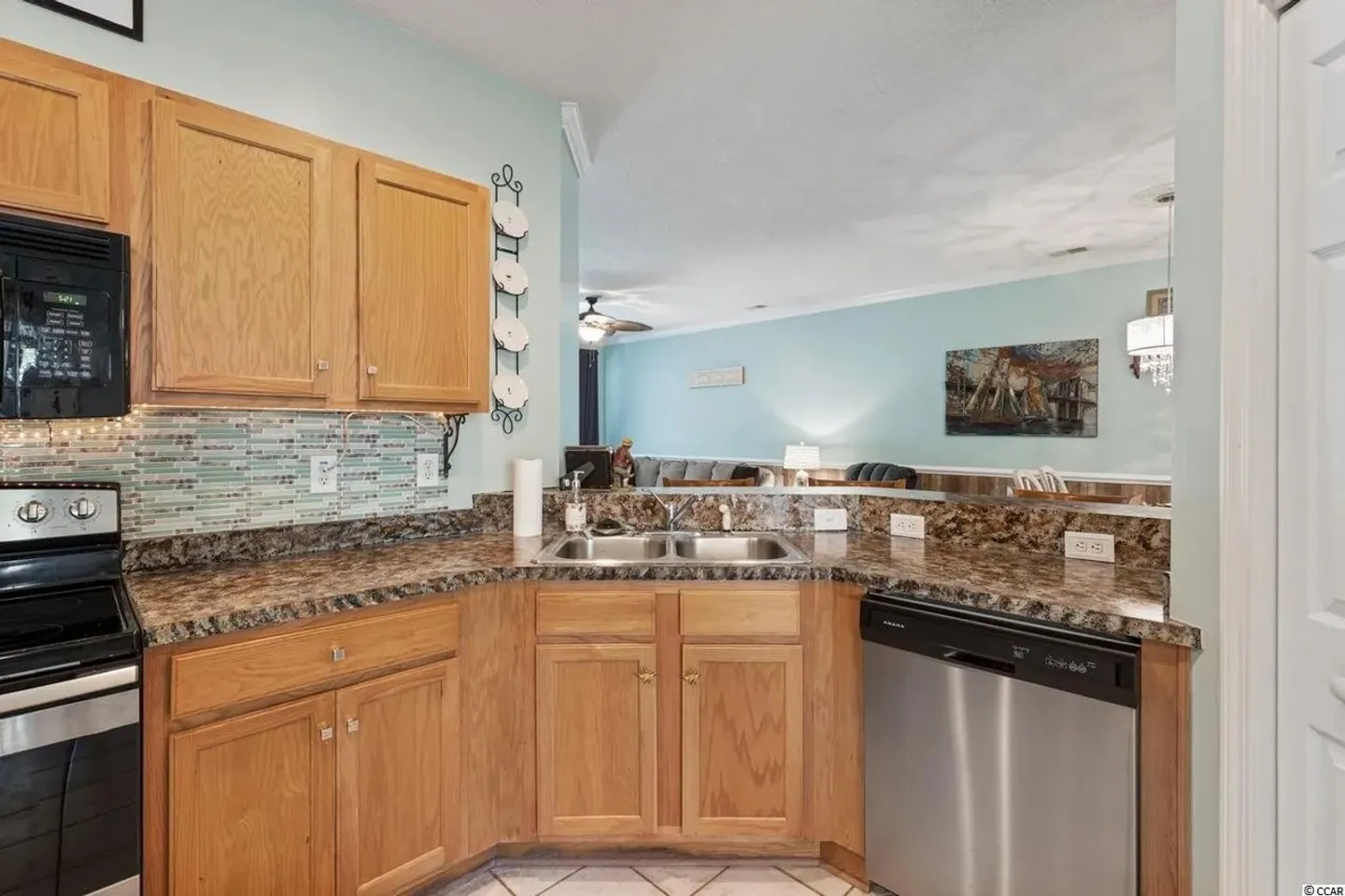 Kitchen counter with stainless steel sink, wood cabinetry, mottled countertop, and a view into the adjacent living room.
