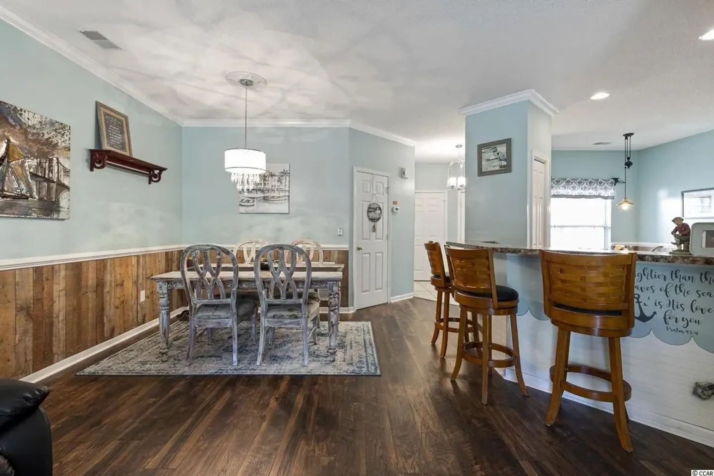 Dining area with wood-look flooring, light blue walls with wood panel wainscoting, and a breakfast bar with wooden stools.