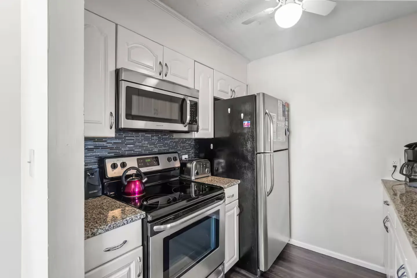 A kitchen with white cabinets, speckled granite-look countertops, a stainless steel microwave and stove, and a full-size refrigerator.