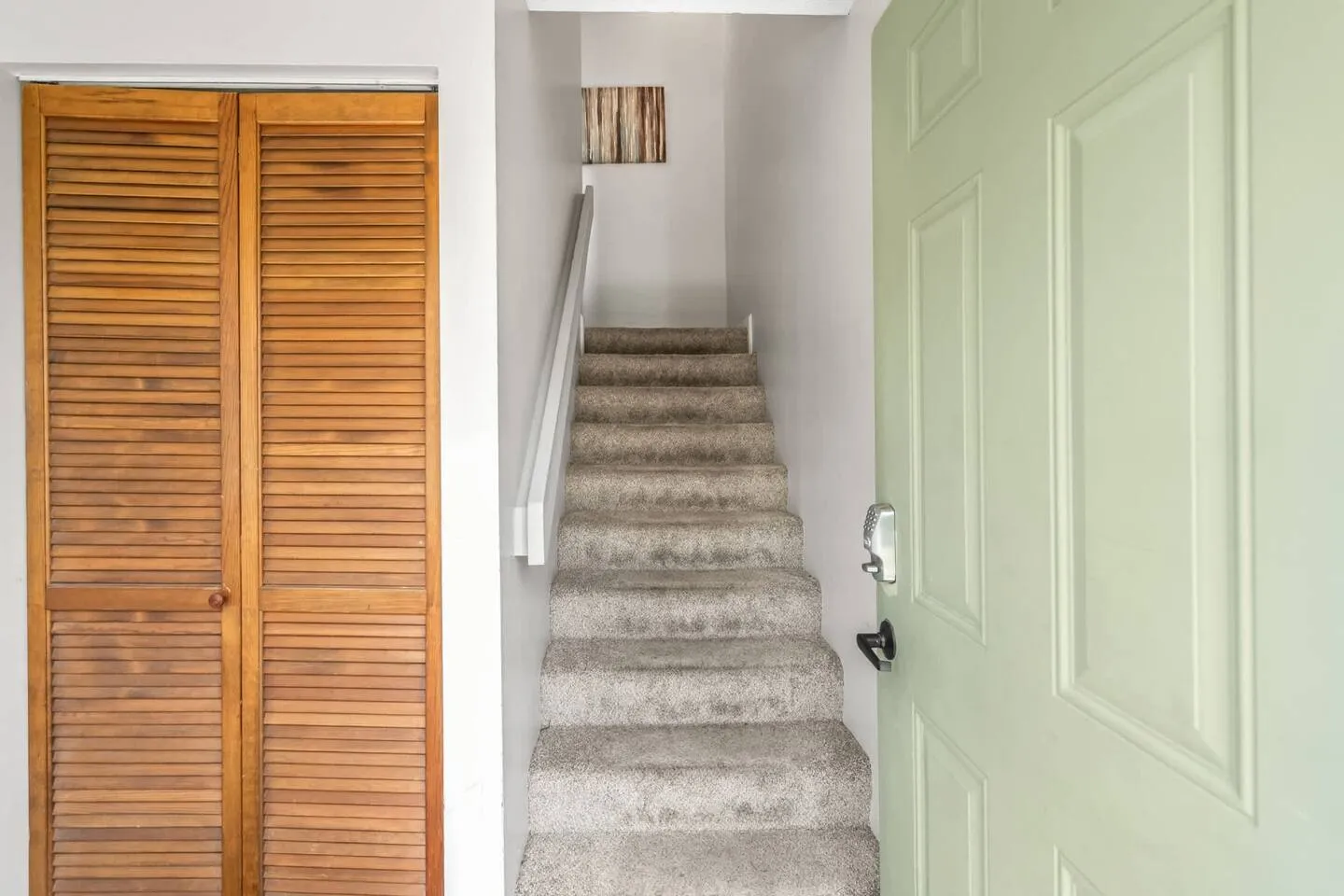 Entryway showing an open pale green front door, a louvered wooden closet door, and carpeted stairs leading up.