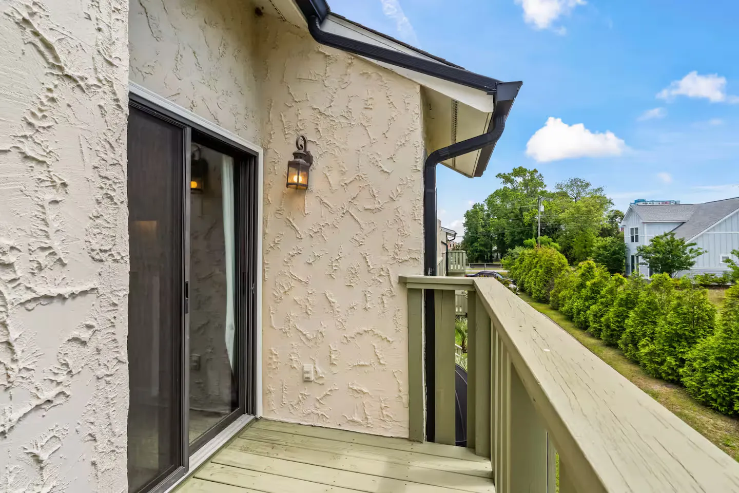 Elevated wooden deck with railing adjacent to sliding glass doors on a stucco house exterior.