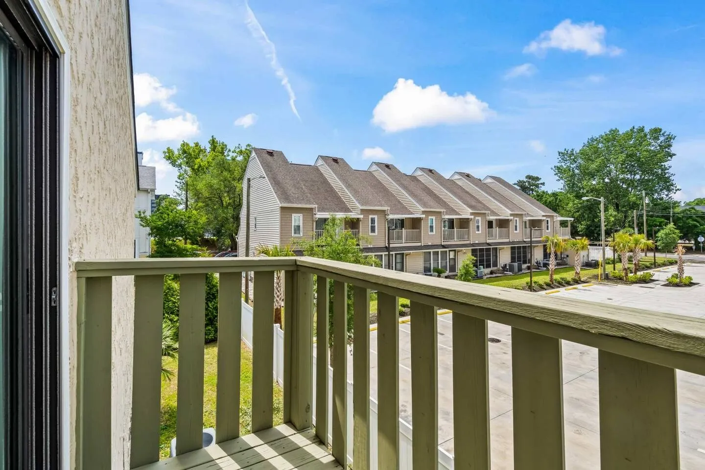 Balcony view overlooking a parking area and neighboring townhomes under a bright blue sky.