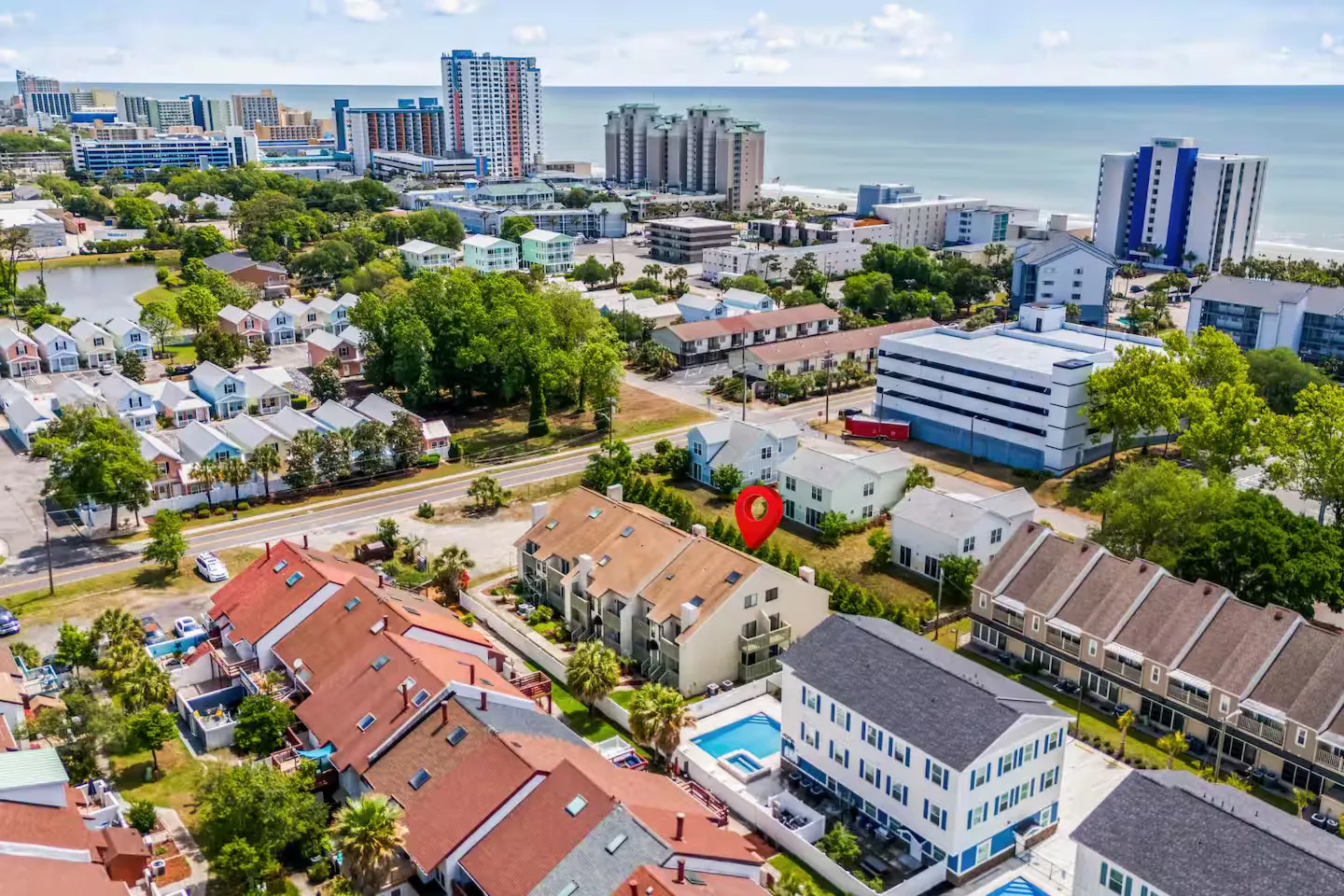 Aerial view of a coastal neighborhood with townhomes, a swimming pool, and the ocean in the background with a red location pin.