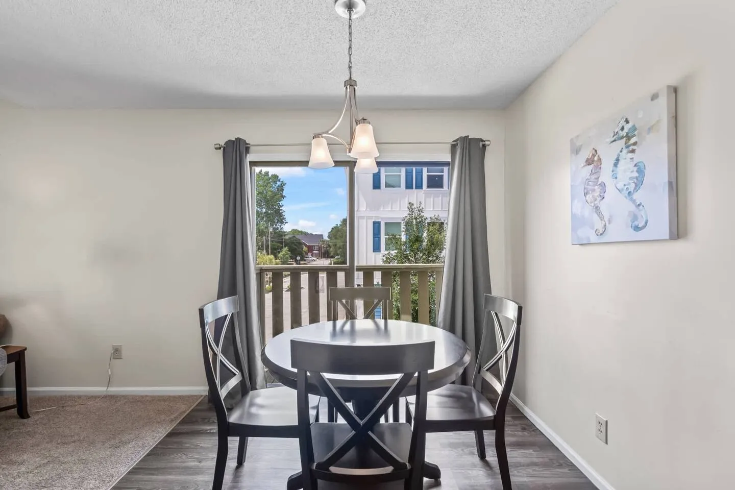 Dining area with a round dark wood table, three visible chairs, a hanging light fixture, and sliding glass doors leading to a balcony.