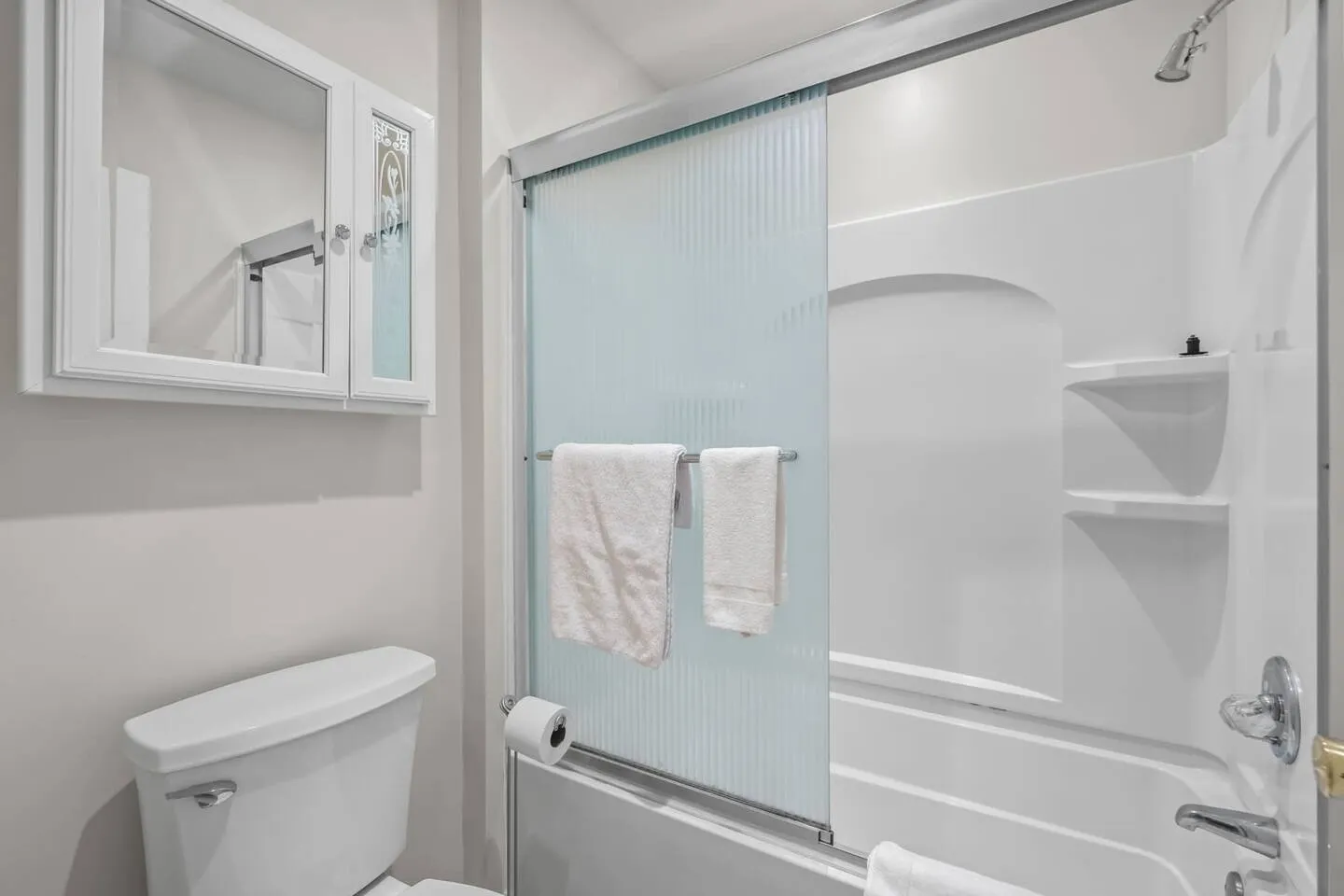 Bathroom showing a white toilet, mirrored medicine cabinet, and bathtub shower combo with frosted sliding glass doors.