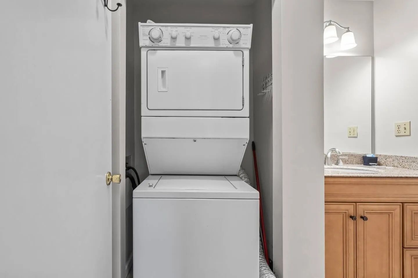 A stacked white washer and dryer unit tucked into a small closet alcove next to a bathroom vanity.