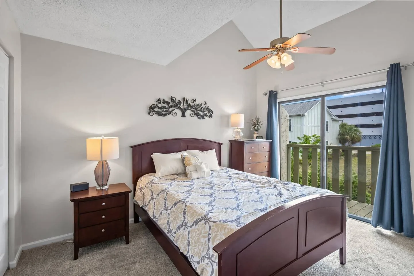Bedroom with vaulted ceiling, wood bed, matching nightstand and dresser, ceiling fan, and sliding glass door leading to a balcony.