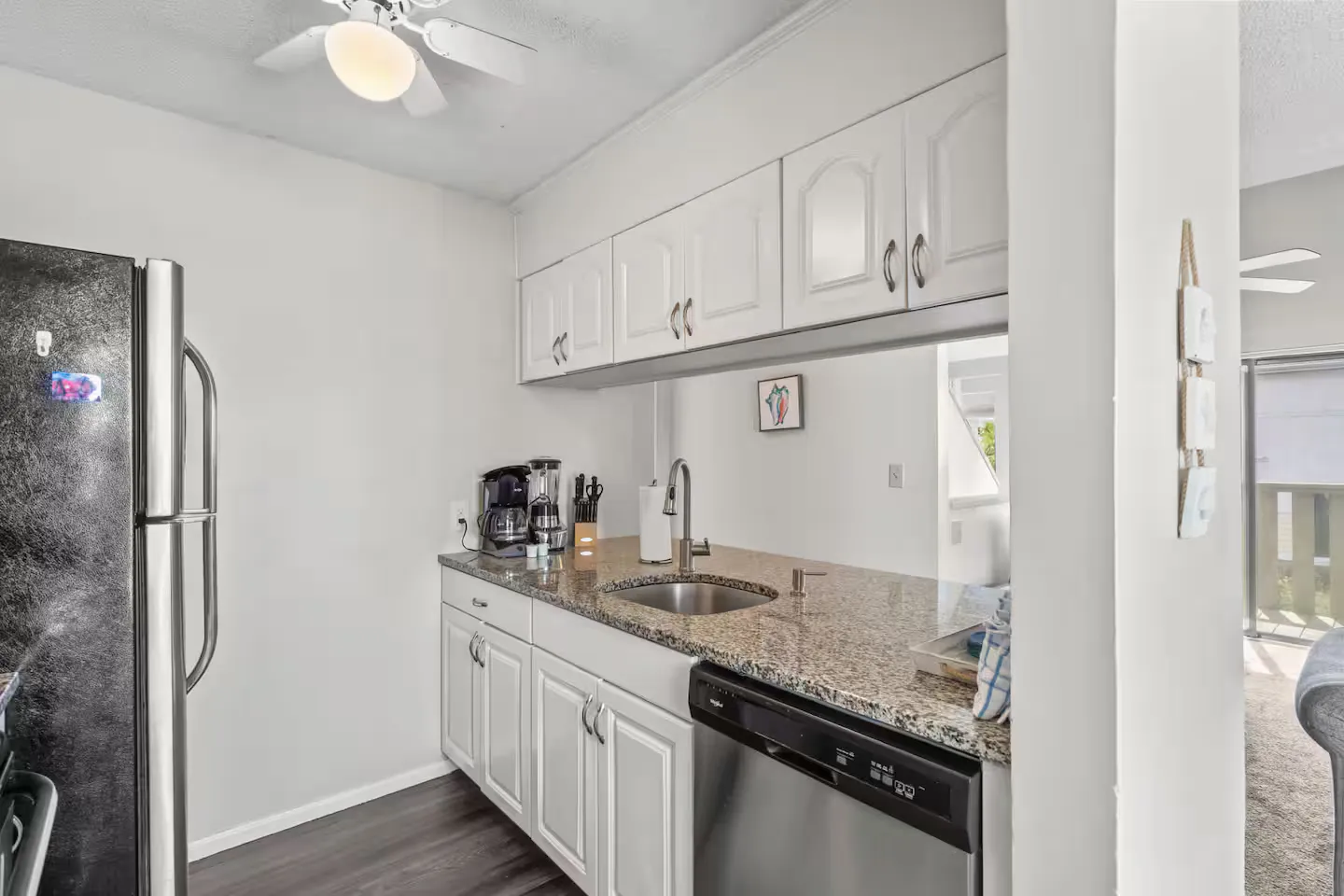 Kitchen featuring white cabinetry, speckled granite countertops, a stainless steel sink, and a built-in dishwasher.