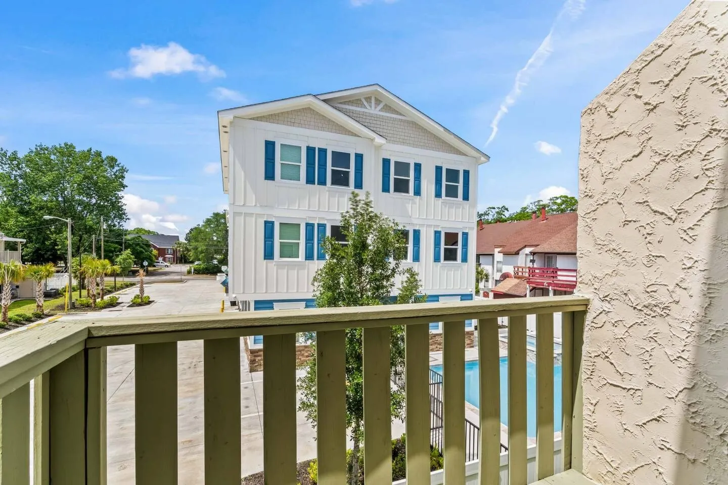 View from an outdoor balcony overlooking a swimming pool and neighboring multi-story residential buildings on a sunny day.