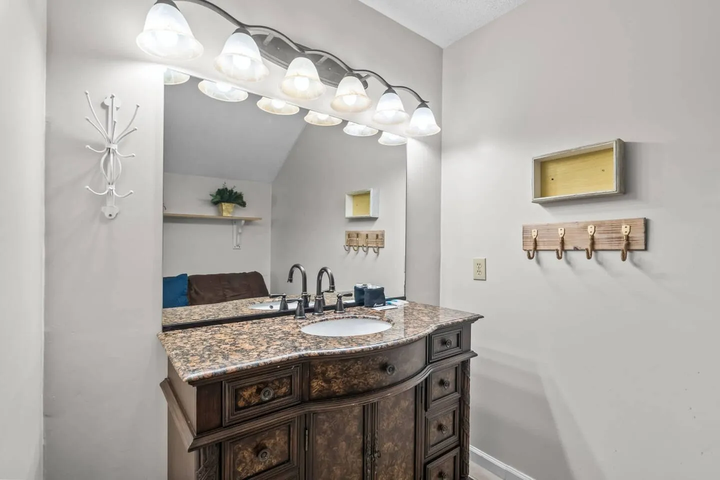 Bathroom vanity with an ornate dark wood cabinet, speckled stone countertop, large mirror, and multi-light vanity fixture.